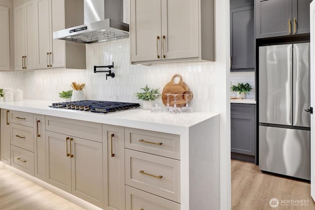 kitchen with stainless steel appliances, light wood-type flooring, light countertops, and wall chimney range hood