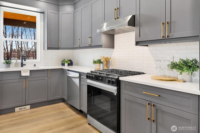 kitchen featuring visible vents, gas range, gray cabinetry, under cabinet range hood, and a sink