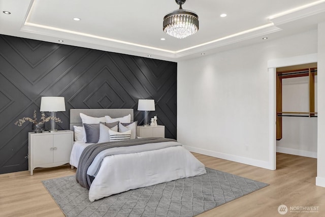 bedroom with baseboards, a raised ceiling, light wood-style flooring, an accent wall, and recessed lighting