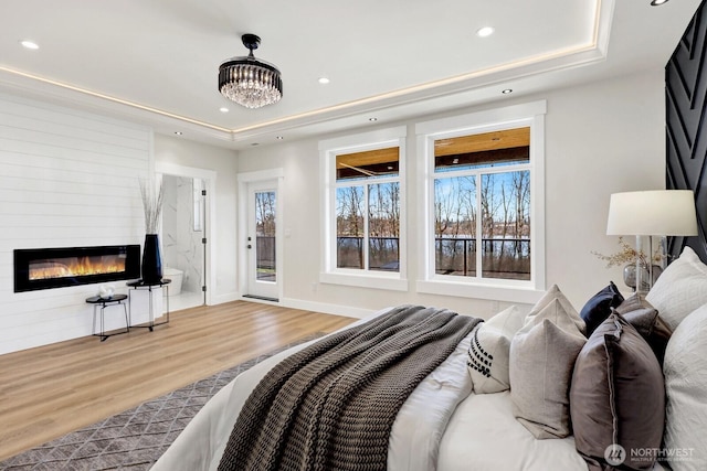 bedroom with a large fireplace, a tray ceiling, and wood finished floors