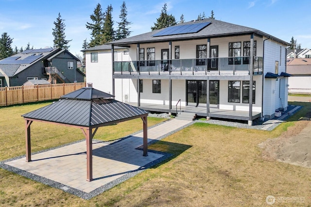 back of property with a patio, a balcony, fence, a lawn, and roof mounted solar panels