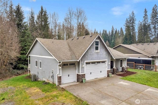 view of front of house featuring a front lawn, stone siding, central AC, roof with shingles, and concrete driveway