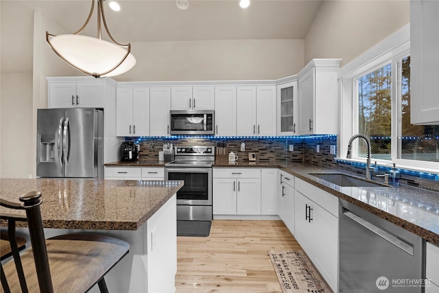 kitchen featuring a sink, stainless steel appliances, light wood-style floors, a kitchen bar, and backsplash