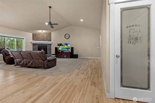 living area with baseboards, vaulted ceiling, a stone fireplace, light wood-style flooring, and a ceiling fan