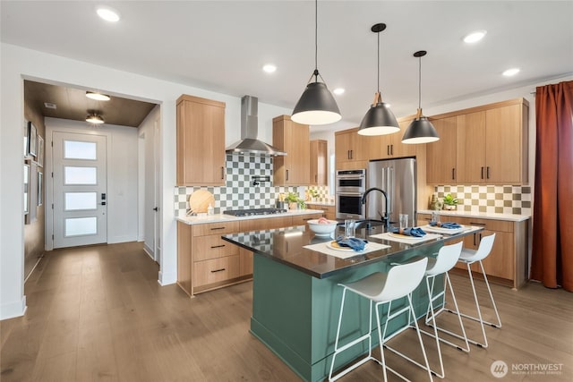 kitchen featuring stainless steel appliances, an island with sink, light wood-style flooring, and wall chimney exhaust hood