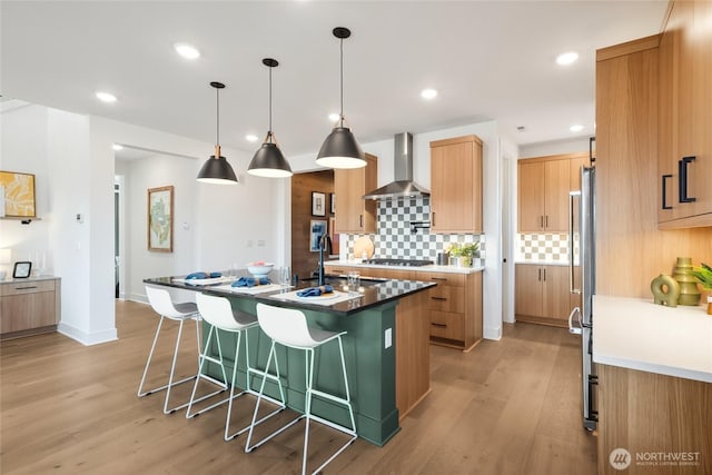 kitchen featuring a breakfast bar, a sink, wall chimney exhaust hood, light wood finished floors, and tasteful backsplash