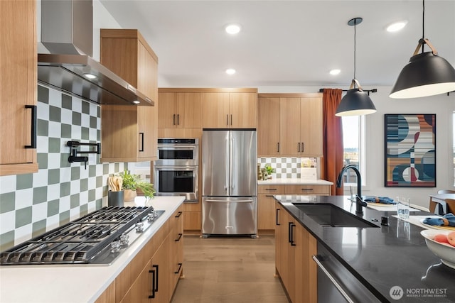 kitchen with light wood-style flooring, a sink, appliances with stainless steel finishes, decorative backsplash, and wall chimney exhaust hood