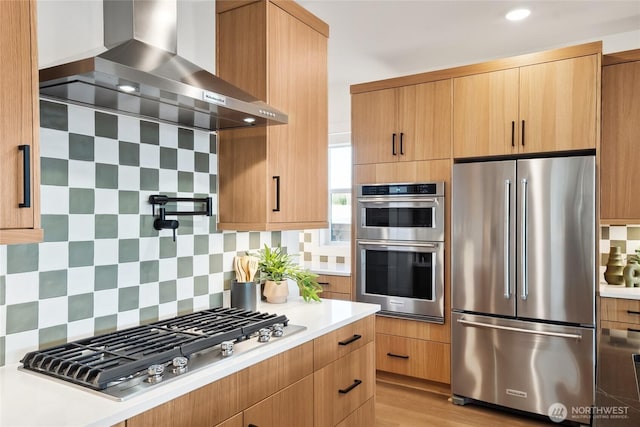 kitchen featuring stainless steel appliances, tasteful backsplash, light countertops, modern cabinets, and wall chimney exhaust hood