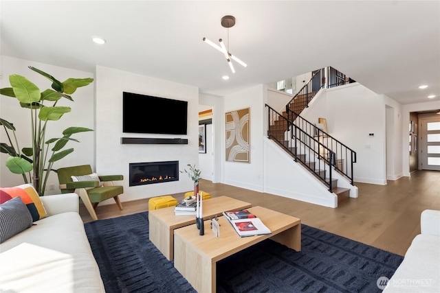 living area with baseboards, a glass covered fireplace, stairway, wood finished floors, and recessed lighting