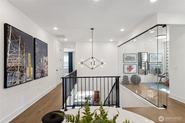 hall featuring visible vents, an upstairs landing, wood finished floors, a chandelier, and baseboards