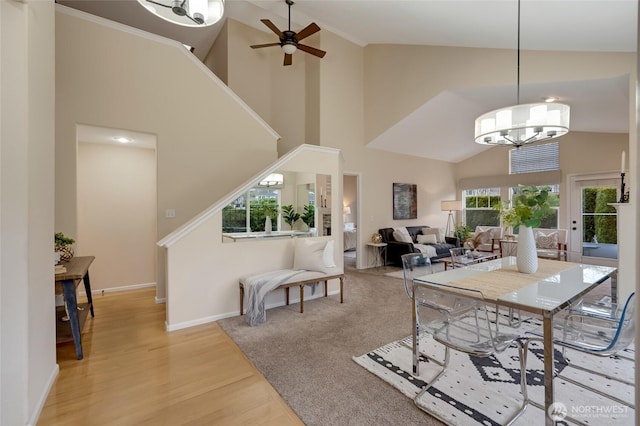 dining space with light wood-style floors, high vaulted ceiling, baseboards, and ceiling fan with notable chandelier