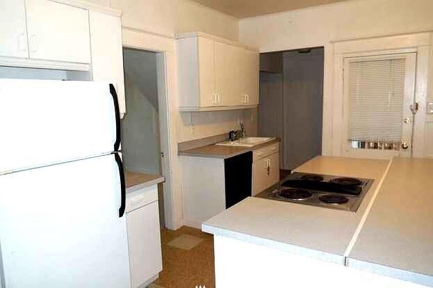 kitchen with light countertops, freestanding refrigerator, white cabinets, stainless steel electric stovetop, and a sink