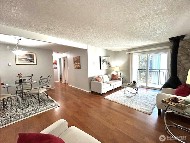 living room with a textured ceiling, wood finished floors, a wood stove, and baseboards