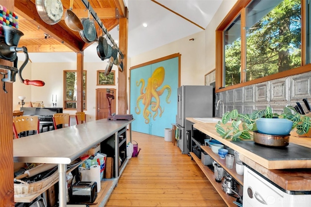 kitchen featuring beam ceiling, open shelves, freestanding refrigerator, a sink, and light wood-type flooring