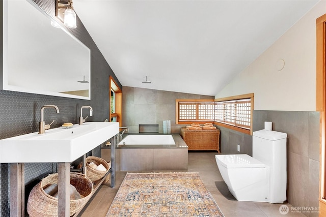 full bath featuring vanity, vaulted ceiling, tile walls, toilet, and a washtub