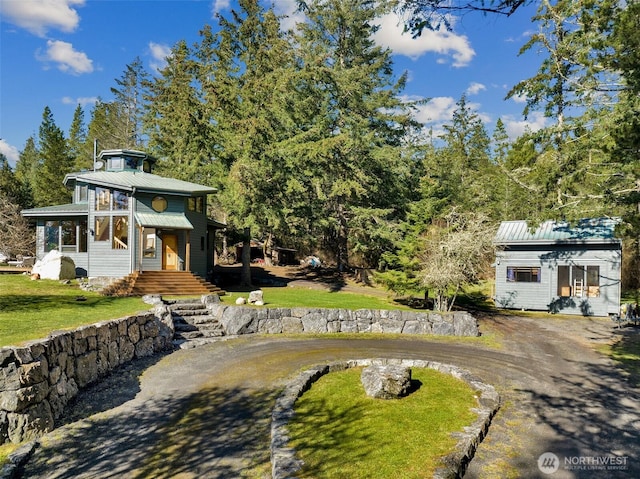 view of front facade featuring a front lawn, dirt driveway, and metal roof