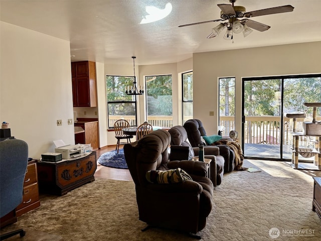 living area featuring dark colored carpet, a healthy amount of sunlight, and ceiling fan with notable chandelier