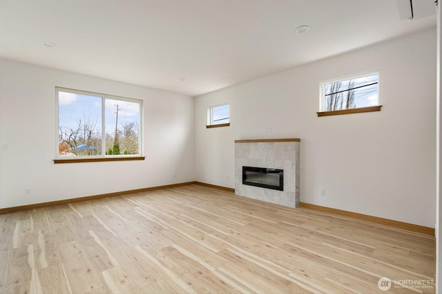 unfurnished living room featuring light wood-style flooring, baseboards, and a tiled fireplace