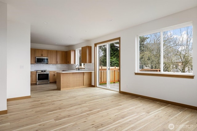 kitchen with baseboards, light wood-style floors, light countertops, appliances with stainless steel finishes, and decorative backsplash