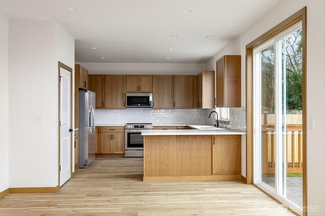 kitchen featuring decorative backsplash, appliances with stainless steel finishes, a peninsula, light wood-type flooring, and a sink