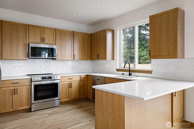 kitchen featuring light wood-style flooring, appliances with stainless steel finishes, a peninsula, light countertops, and a sink