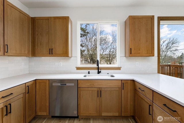 kitchen featuring a sink, light countertops, stainless steel dishwasher, decorative backsplash, and brown cabinetry