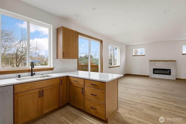 kitchen with light wood finished floors, dishwasher, a peninsula, light countertops, and a sink