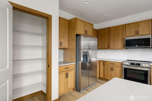 kitchen with light countertops, decorative backsplash, appliances with stainless steel finishes, brown cabinetry, and light wood-type flooring