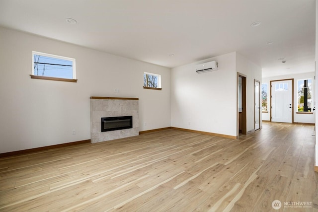 unfurnished living room featuring light wood-style floors, baseboards, a wall unit AC, and a tiled fireplace