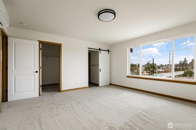 unfurnished bedroom with a barn door, light carpet, baseboards, a spacious closet, and a wall mounted AC