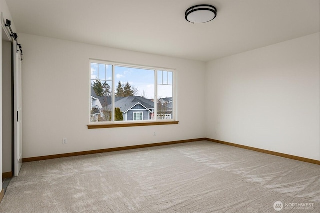 carpeted spare room featuring a barn door and baseboards