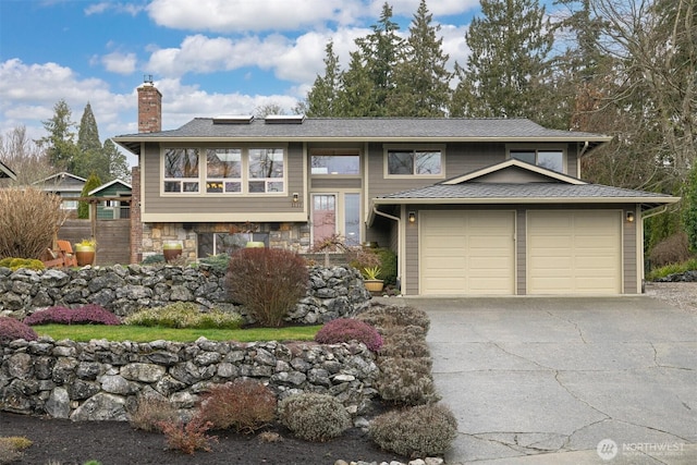 split foyer home with an attached garage, driveway, a chimney, and stone siding