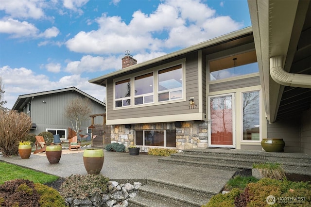 exterior space with a patio, a chimney, and stone siding