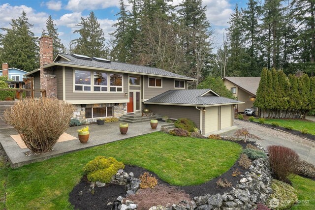 bi-level home featuring driveway, stone siding, a chimney, an attached garage, and a front yard