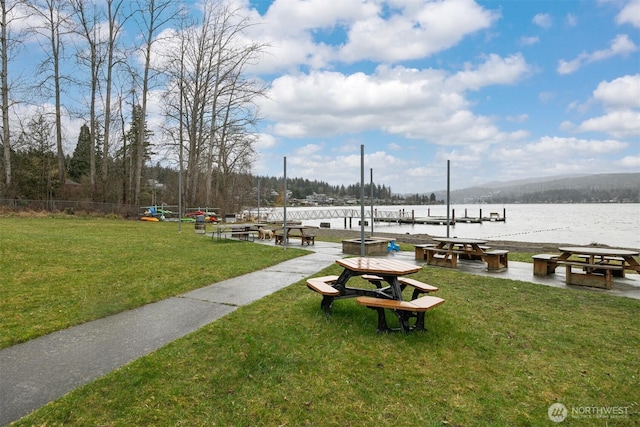 view of property's community with a dock, a water view, a lawn, and fence