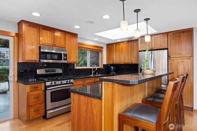 kitchen with brown cabinetry, appliances with stainless steel finishes, a kitchen breakfast bar, light wood-style floors, and a sink