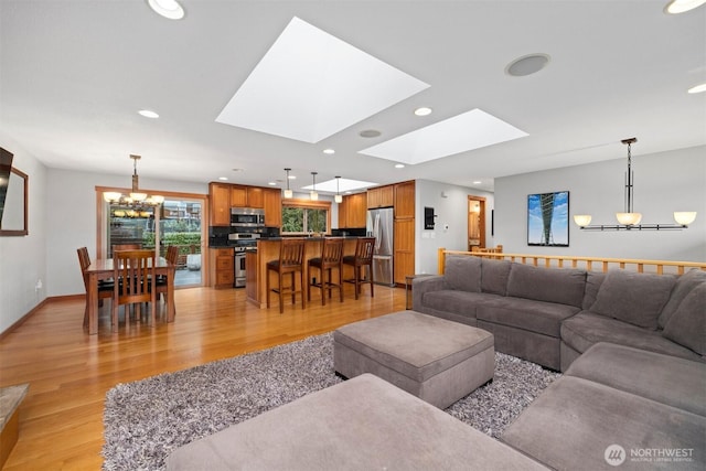 living area featuring a skylight, recessed lighting, an inviting chandelier, light wood-style floors, and baseboards