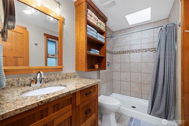 full bath with a stall shower, a skylight, vanity, and toilet