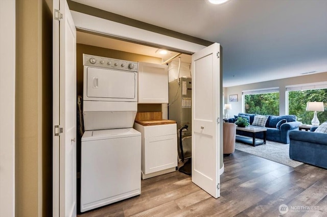 washroom with stacked washing maching and dryer, cabinet space, and wood finished floors