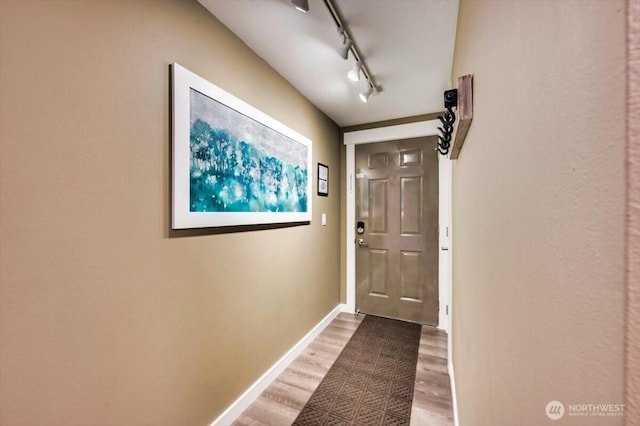 entryway with wood finished floors, rail lighting, and baseboards