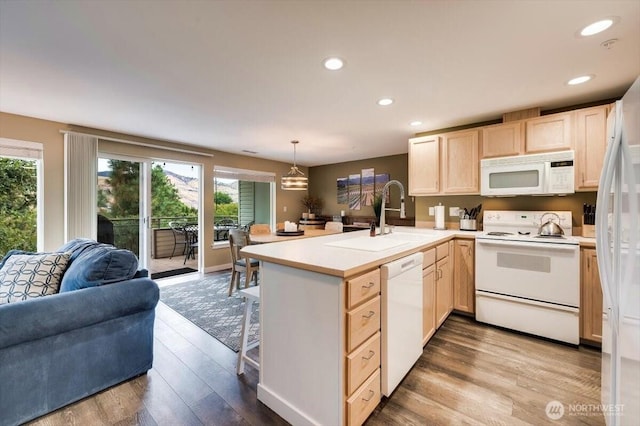 kitchen with light brown cabinetry, open floor plan, a sink, white appliances, and a peninsula