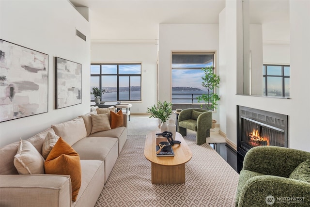 carpeted living room featuring a warm lit fireplace, heating unit, visible vents, and baseboards