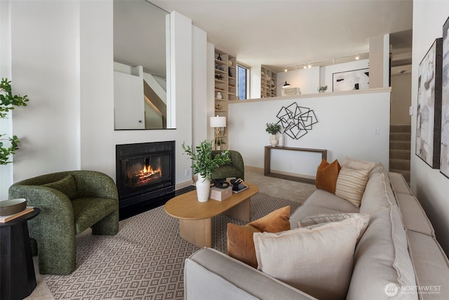 living area with carpet floors, a glass covered fireplace, stairway, and track lighting