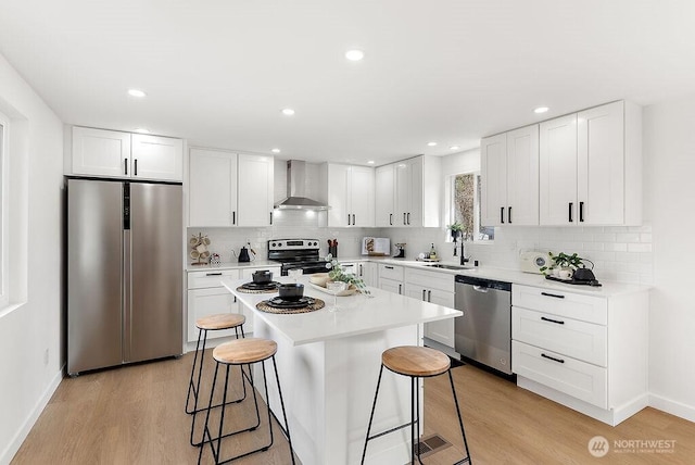 kitchen featuring a breakfast bar area, stainless steel appliances, a sink, light wood-type flooring, and wall chimney exhaust hood