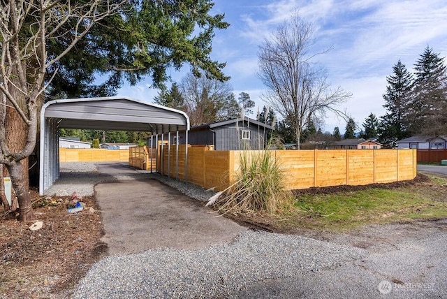 view of side of home with driveway, a fenced front yard, and a detached carport