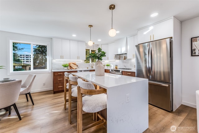 kitchen with a kitchen island, appliances with stainless steel finishes, light countertops, light wood-style floors, and a kitchen bar