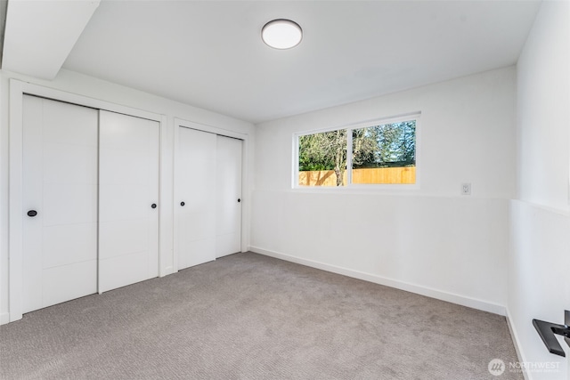 unfurnished bedroom with carpet floors, two closets, and baseboards