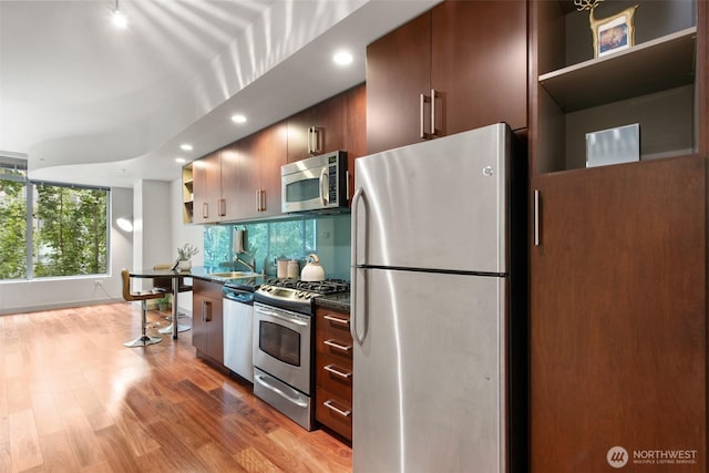 kitchen with dark countertops, light wood-style flooring, appliances with stainless steel finishes, open shelves, and a sink