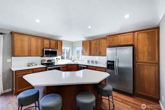 kitchen with appliances with stainless steel finishes, a breakfast bar, brown cabinets, and a sink