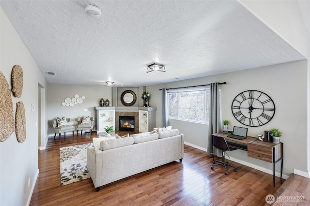 living room with visible vents, a textured ceiling, a tiled fireplace, and wood finished floors